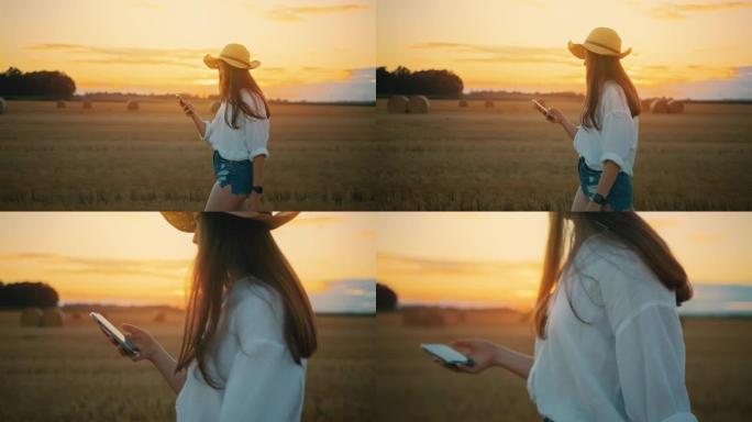 SLO MO年轻女子在日落时分走在田野里时使用智能手机