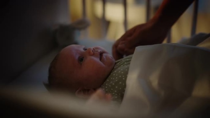 真实的特写镜头，一位母亲在婴儿床中抚慰并牵着新生婴儿的手。白人新生儿蹒跚学步的孩子在孩子们的卧室里。