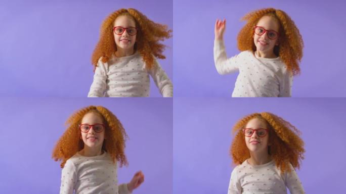 工作室拍摄的红发年轻女孩戴着红色眼镜跳舞，在紫色背景下玩得开心 -- 慢动作拍摄