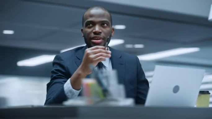 360学位办公室: 成功的黑人商人坐在办公桌前思考，使用笔记本电脑。非裔美国企业家做股市投资分析四处