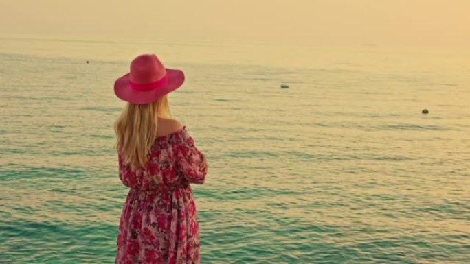 赫瓦岛 (Hvar island) 傍晚站在海上的金色头发，粉红色帽子和连衣裙的女人