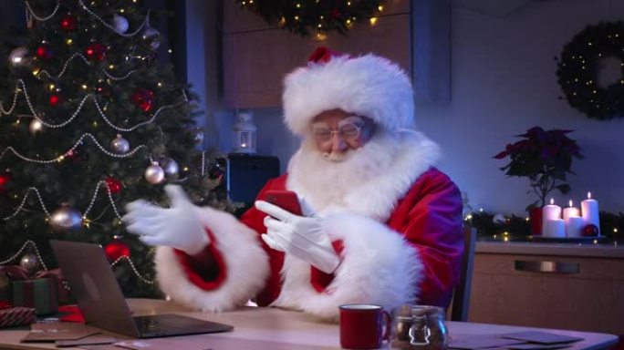 圣诞老人正在使用智能手机通过视频链接与坐在客厅里一张大桌子上的孩子们交谈。
