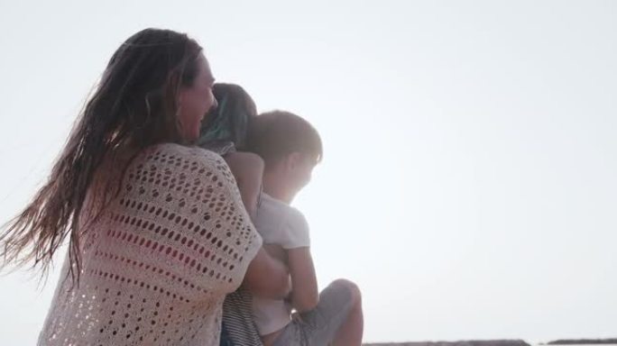 爱情和家庭度假，年轻快乐的母亲在夏天的沙滩上慢动作中抱着两个快乐的孩子旋转