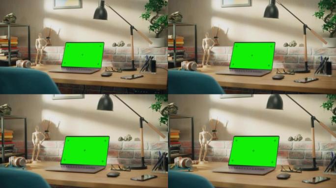 笔记本电脑站在木桌上，绿屏Chromakey模拟显示器。舒适的空阁楼公寓，桌子上有一盏灯、笔记本和智