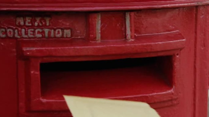 一个年轻人的手发送邮件，将一封信张贴到英国的邮箱中。特写。