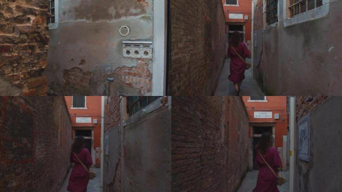 电影摄影机跟随穿着紫色连衣裙的年轻女子沿着威尼斯老建筑之间非常狭窄的通道行走。