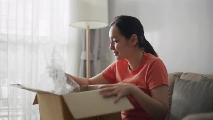 年轻亚洲女性消费者打开纸板箱获得邮政包裹