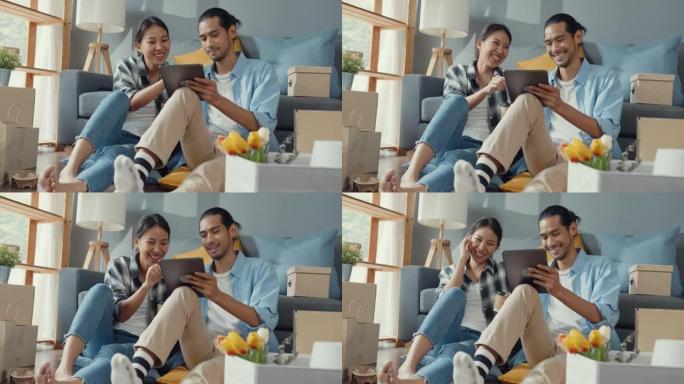 快乐的亚洲年轻迷人的夫妇使用平板电脑网上购物家具装饰房子用纸箱包装搬到新房子里。