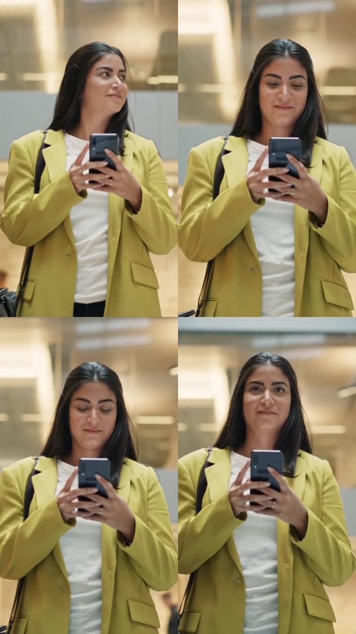 垂直镜头: 一位拉丁妇女看着她的智能手机并在公司办公楼中行走的肖像。女商人在加薪时微笑着。跟踪慢动作