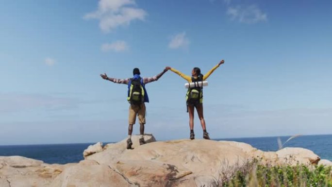 徒步旅行时，非洲裔美国夫妇站在岩石上，双臂张开