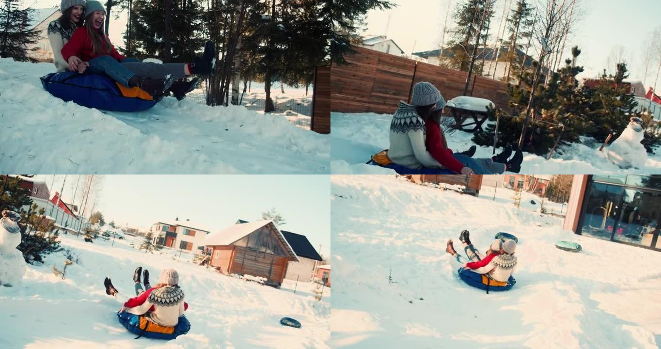 两个迷人的快乐年轻女人在雪坡上向阳光明媚的房子微笑着雪橇。寒假休闲慢动作。