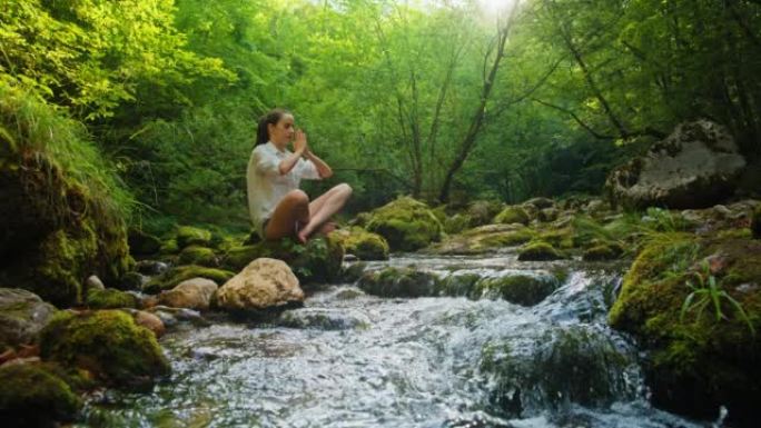 SLO MO年轻女子在溪流边的岩石上练习瑜伽