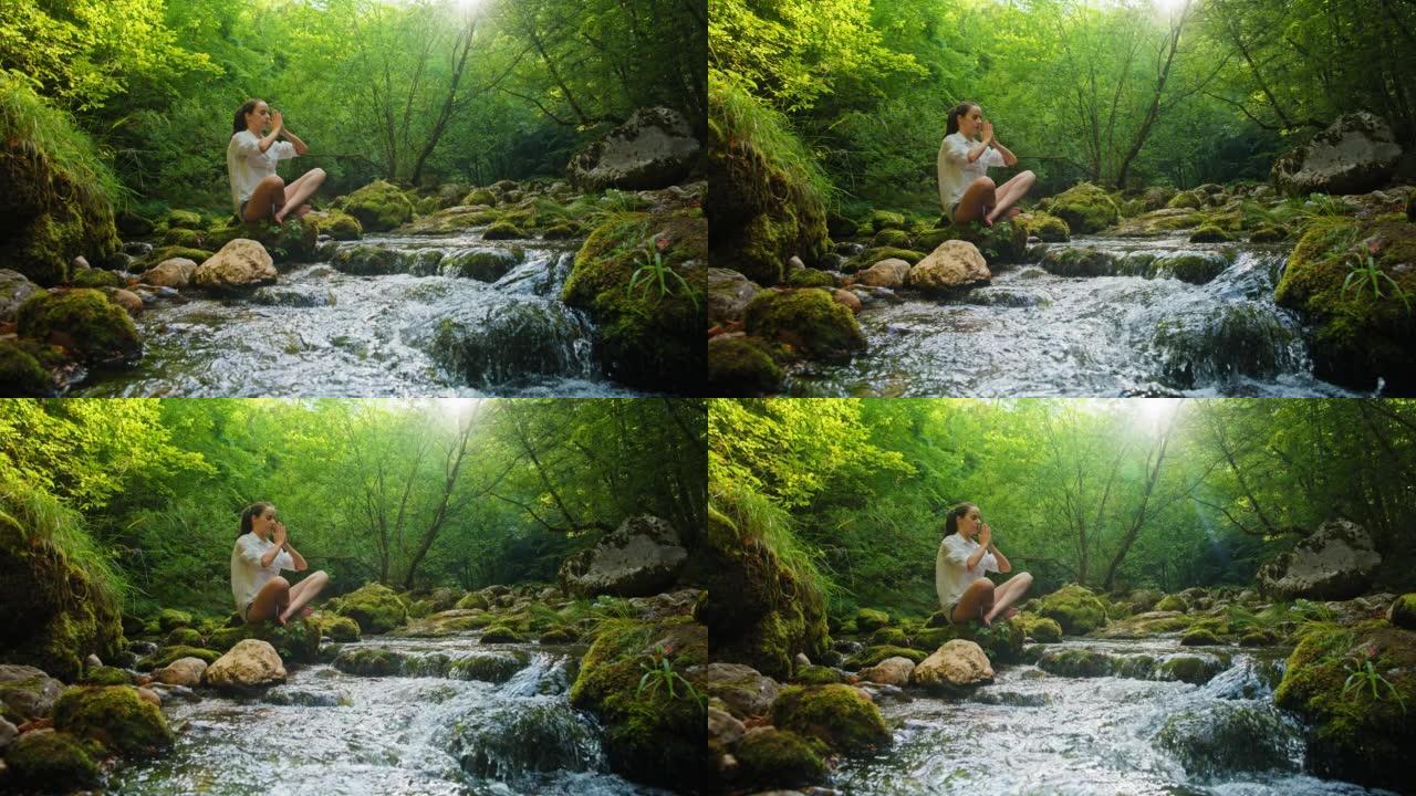 SLO MO年轻女子在溪流边的岩石上练习瑜伽