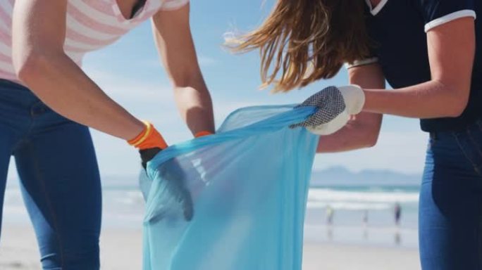 两个不同的女性朋友在海滩上将垃圾放在垃圾袋中