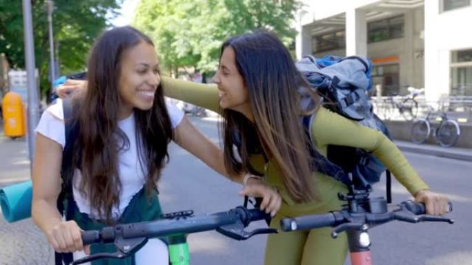 在城市中，两名女背包客带着踏板车