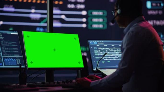 专业的信息技术技术支持专家和软件开发人员在数字屏幕监控控制室的绿屏模拟显示计算机上工作。员工戴上耳机