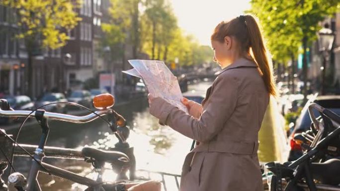 微笑的女人拿着阿姆斯特丹的地图，站在运河旁边，在美丽的晴天欣赏风景