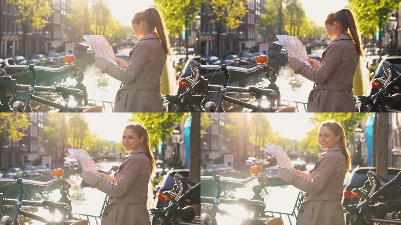微笑的女人拿着阿姆斯特丹的地图，站在运河旁边，在美丽的晴天欣赏风景