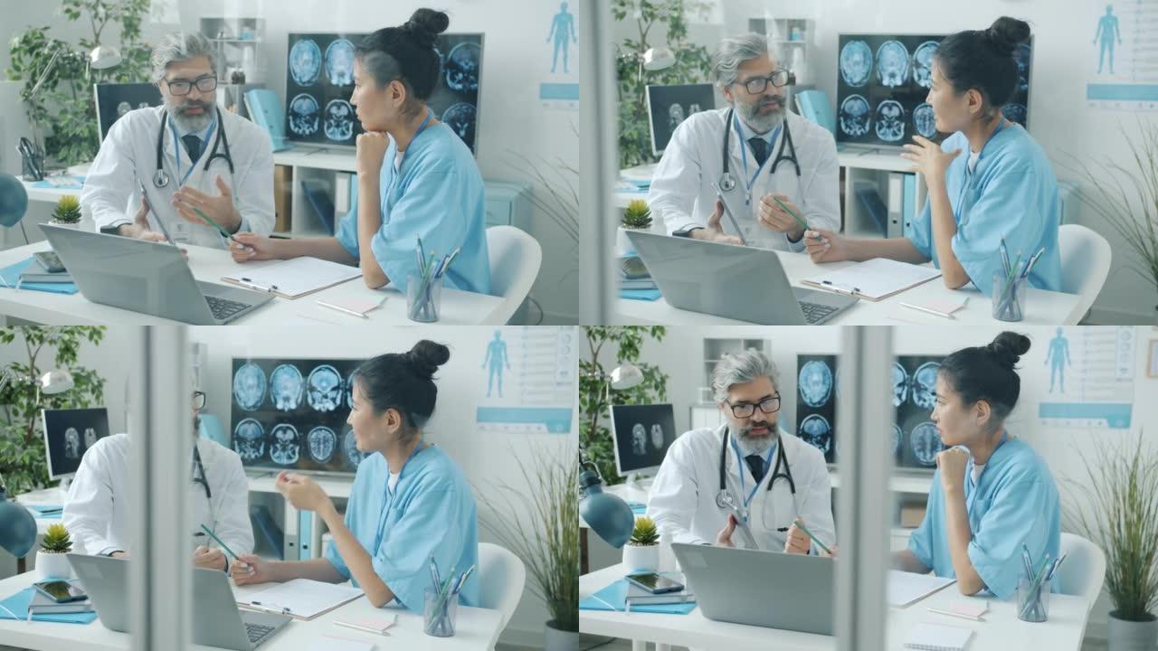 经验丰富的医生与护士交谈，显示在医院办公室工作的平板电脑屏幕