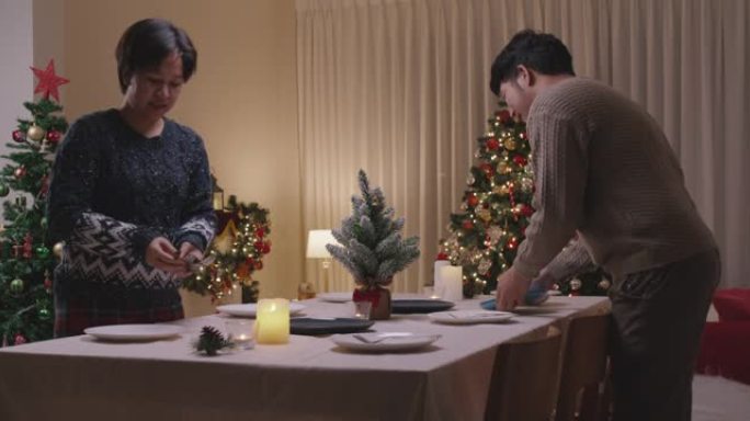 亚洲夫妇为今晚的派对准备圣诞夜餐桌设置。