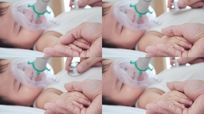 亚洲小男孩生病，戴着吸入器口罩和医生检查心脏，以防止流行病，睡觉的婴儿的手在床上的母亲的手。