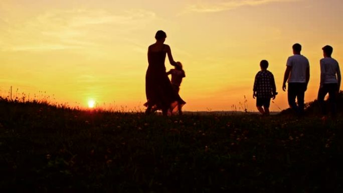 日落时在草地上放松的年轻家庭的SLO MO剪影
