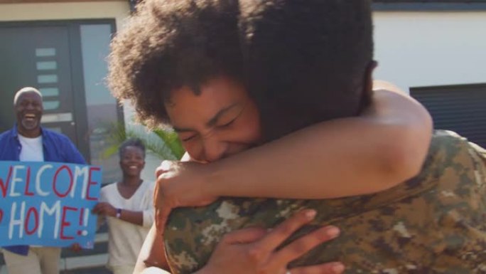 几代人的家庭，父母和妻子在房子外面用横幅和标语欢迎休假的军人回家，他拥抱妻子——慢镜头拍摄