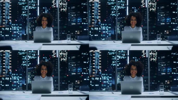 深夜，一位成功的非洲裔美国女商人在大城市办公室的笔记本电脑上工作的肖像。穿着时髦的蓝色衬衫的黑人头发