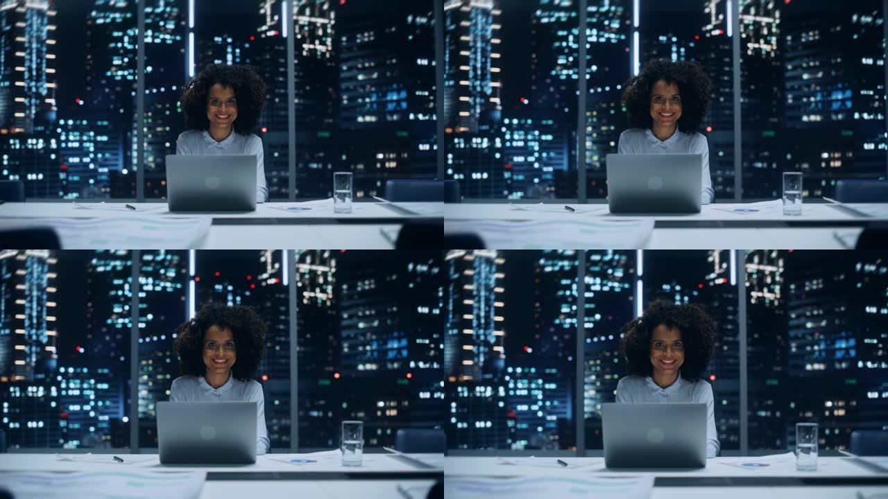 深夜，一位成功的非洲裔美国女商人在大城市办公室的笔记本电脑上工作的肖像。穿着时髦的蓝色衬衫的黑人头发