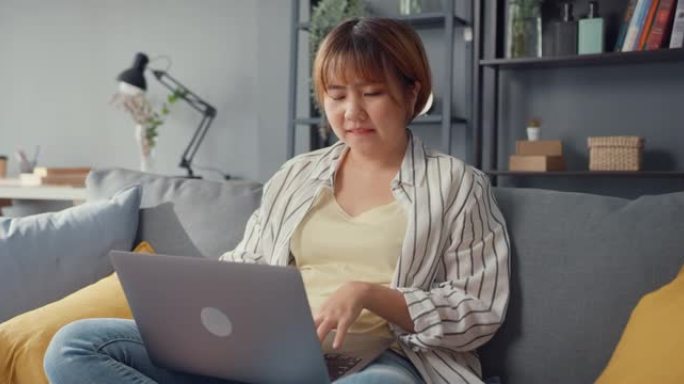 自由亚洲女士休闲服使用笔记本电脑在线学习在家里的客厅。