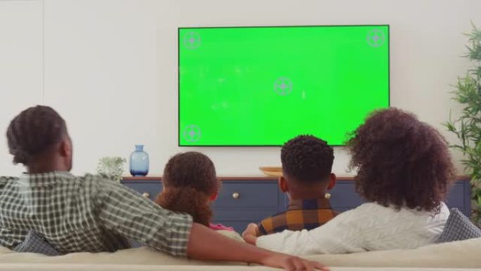 家庭坐在沙发上的后视图在家里的绿屏电视上看恐怖电影