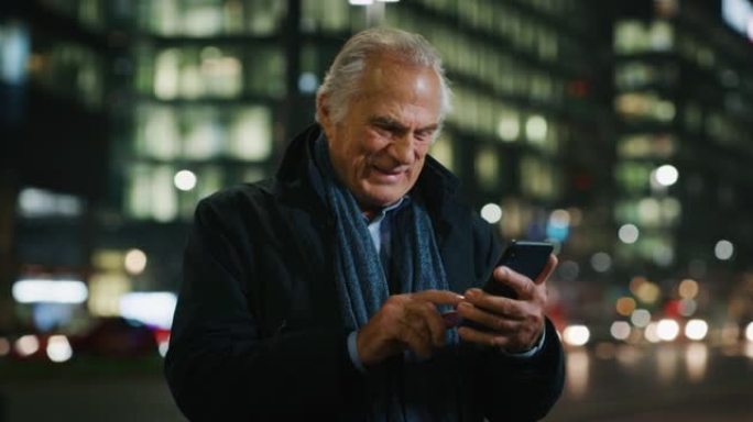 一个英俊的高级男人晚上在城市中心使用手机。