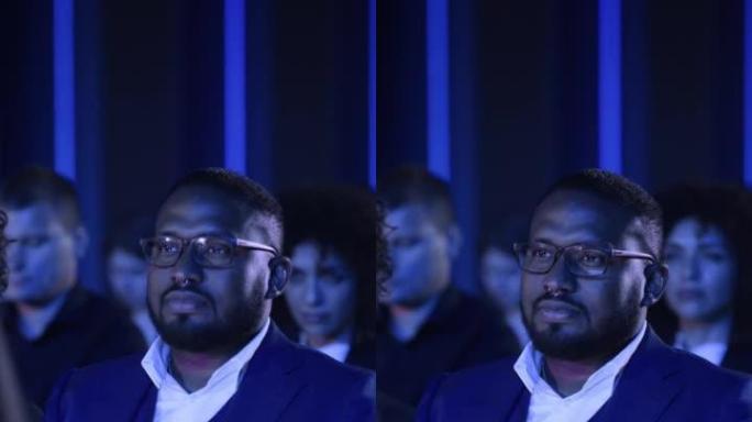垂直屏幕: 非洲男性坐在科技会议上黑暗拥挤的礼堂里。专业使用笔记本电脑。专家观看有关新软件解决方案的
