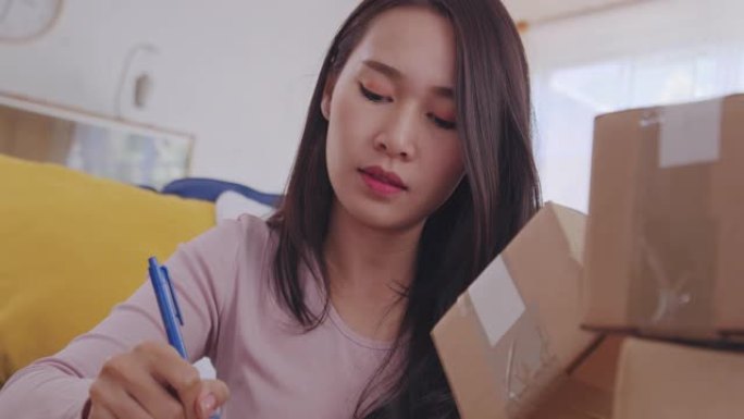 手持和特写镜头年轻的亚洲女性工作和箱子包装或完成零售订单，密封纸板箱准备在家里做生意时装运。女性在客