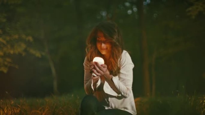 SLO MO女人在黄昏时在薄雾笼罩的森林中拿起一盏小电灯