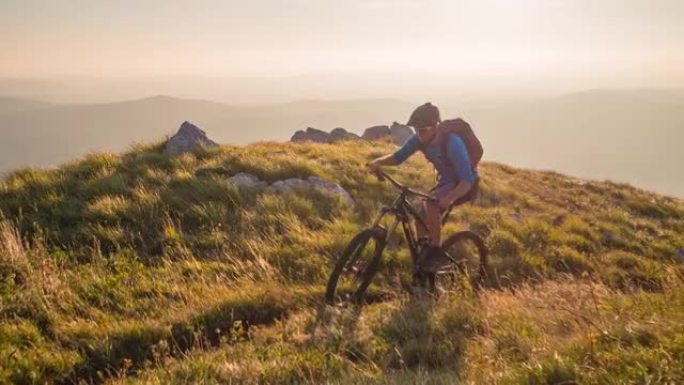 在大自然的户外运动，山地自行车上坡，日落时被绿色的草地和山脉包围