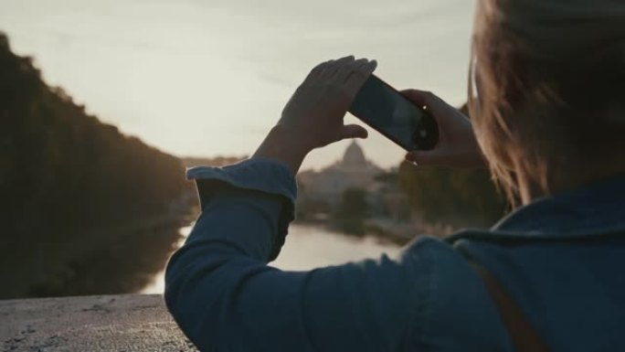 SLO MO女人在日落时使用智能手机为圣天使桥拍照