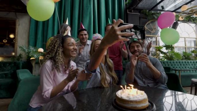 美丽的生日女人用智能手机录制视频，而她的朋友在餐厅唱歌并庆祝她的生日