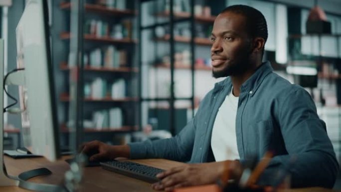 英俊的黑人非洲裔美国专家在创意家居客厅从事台式电脑工作。自由职业者男性正在为客户和雇主编写财务演示报