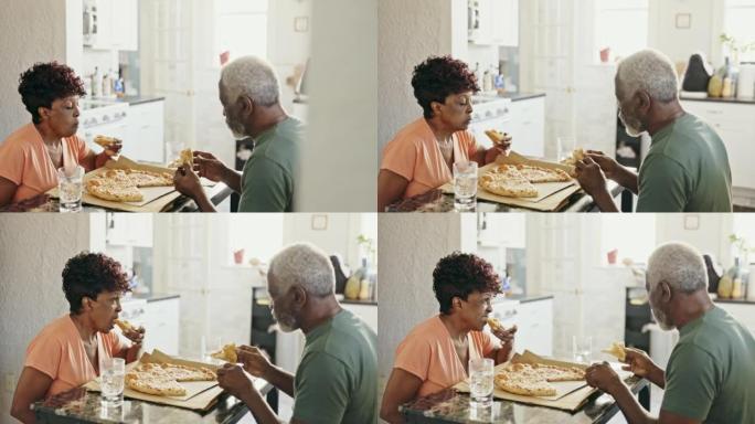 放松的高级夫妇在厨房餐桌上吃披萨