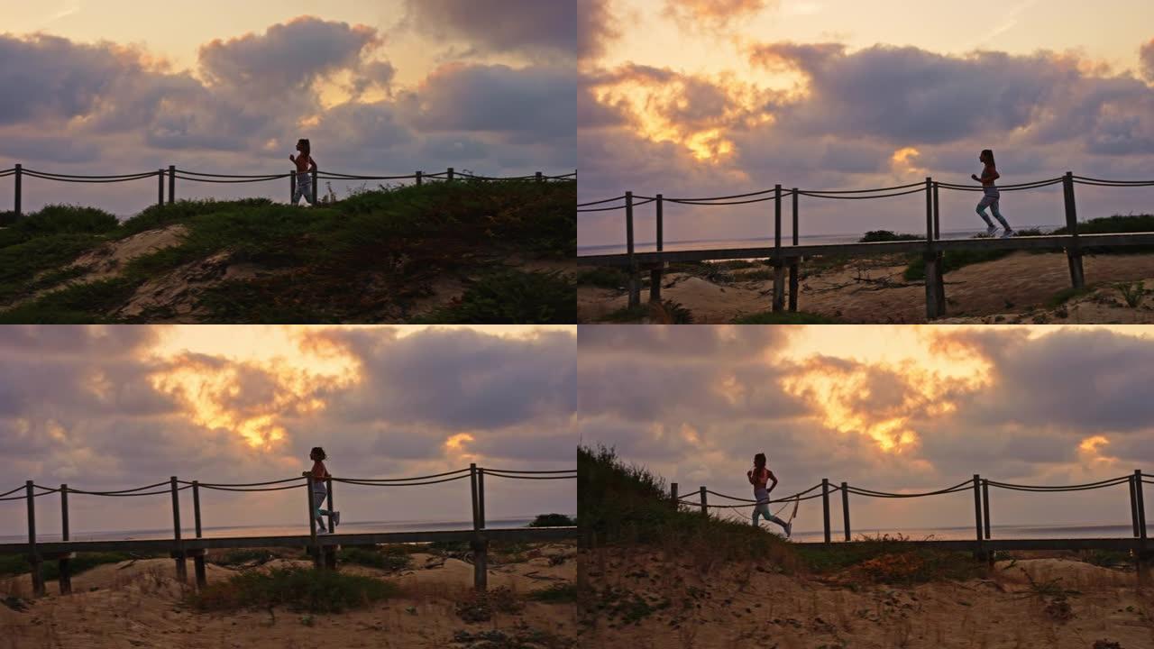 在日落期间，在海滩上的木板路上奔跑的无法识别的女运动员的跟踪慢动作镜头