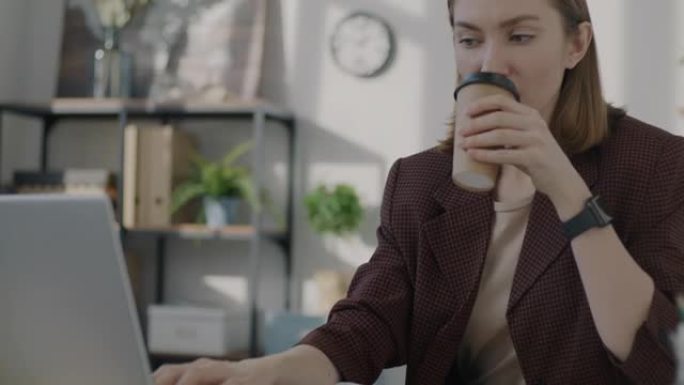 女性上班族在工作场所使用笔记本电脑工作和喝酒去喝咖啡