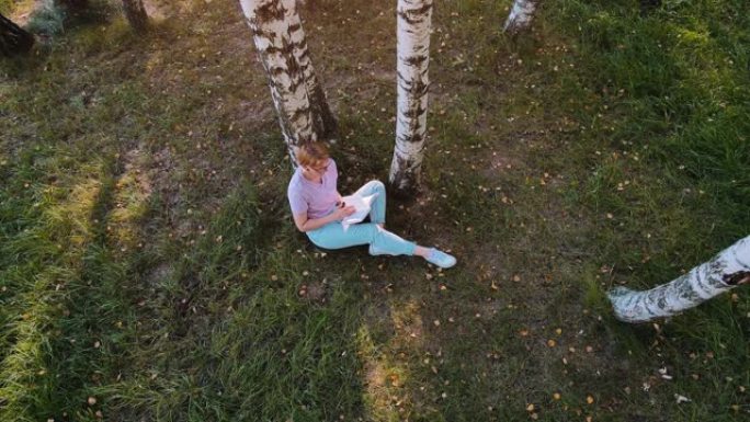 女人坐在外面的桦树附近看书