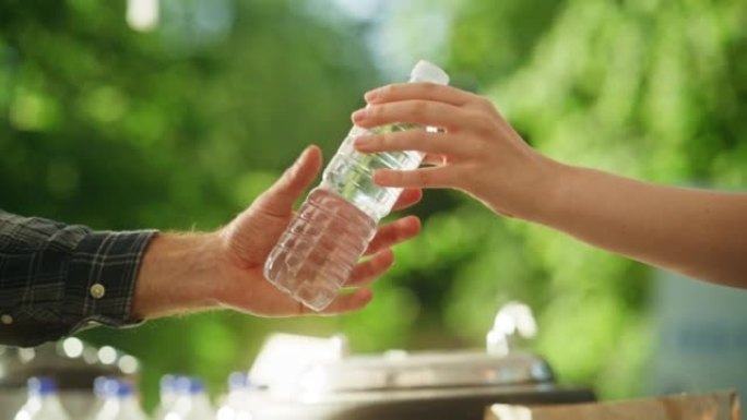 一个匿名的人把水瓶交给另一个人的特写镜头。大自然中的绿色背景。户外四庭卖饮料。生态、医疗保健和水合概