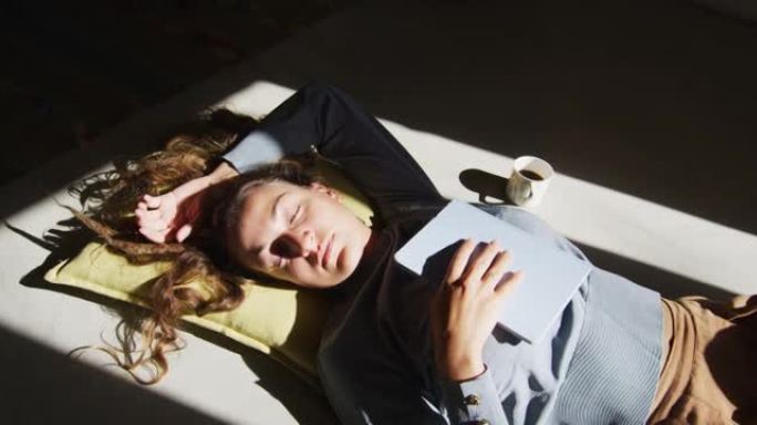 白人妇女躺在地板上拿着书，睡在阳光明媚的小屋客厅