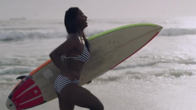 4k视频片段，一位迷人的年轻女子拿着冲浪板沿着海滩奔跑