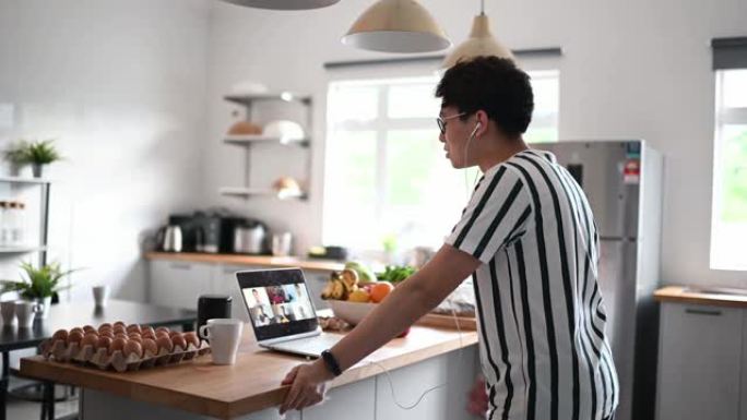 亚洲chhinese年轻成年男子在家庭厨房柜台视频会议与他的朋友休闲服装使用笔记本电脑