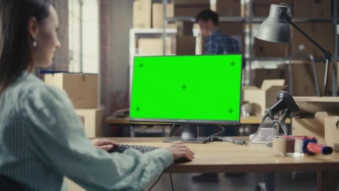 女性使用带有绿屏Chromakey模拟显示的台式计算机。销售经理和在配送仓库工作的员工用纸箱。肩膀上