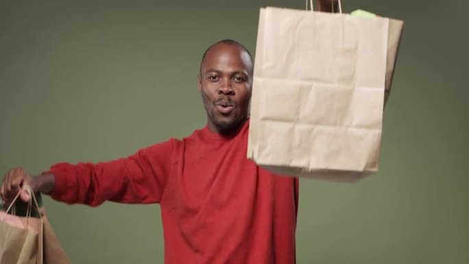 一个快乐的黑皮肤男人用装有礼物盒的彩色袋子举起双手