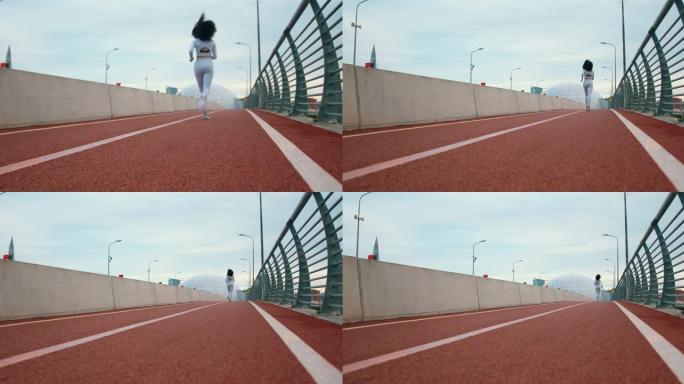 一个穿着白色运动服的健美卷发女跑步者正在桥上慢跑，我们从后面看到她的慢动作